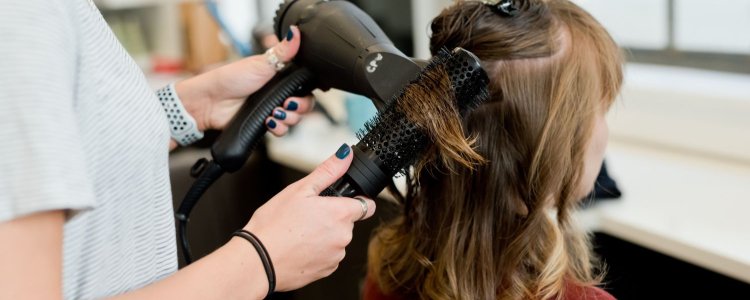O cabeleireiro seca e os estilos recém -cortados no salão; A cabeleireira tem unhas azuis e seu cliente tem cabelos castanhos avermelhados