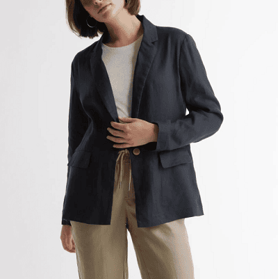 Mulher inclina a cabeça enquanto usava um blazer de linho marinho, calças bege e uma camiseta branca