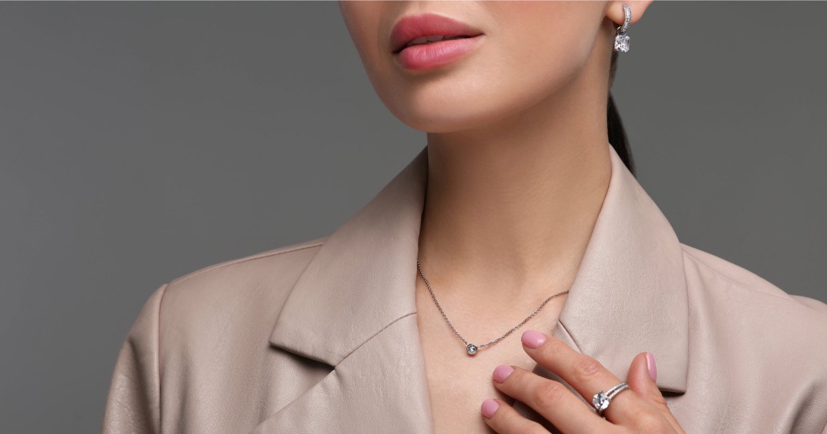 mulher profissional de terno bege usa colar, anel e brincos; ela está pensando em quais joias são apropriadas para o escritório em 2026