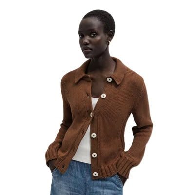 Uma mulher vestindo um cardigã marrom, blusa branca e calça jeans