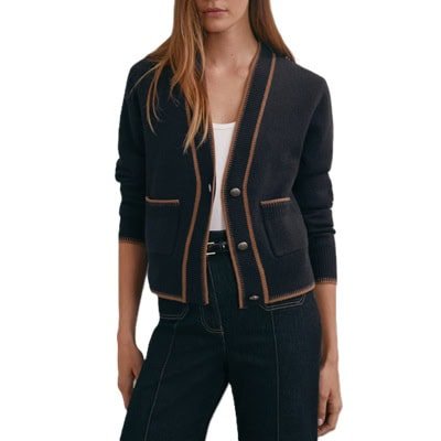 Uma mulher vestindo calça preta, faixa preta, blusa branca e cardigã de bolso azul marinho com detalhes marrons