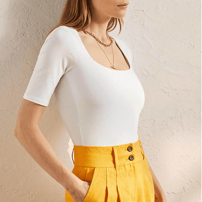 camiseta branca opaca com gola redonda e mangas na altura do cotovelo; estilizado com calça plissada amarela de cintura alta
