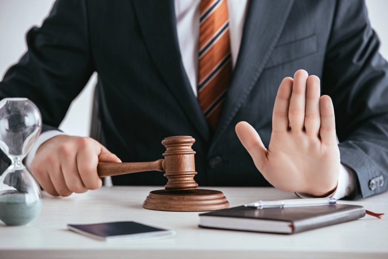 Homem de terno com martelo de juiz numa mão e a outra mão levantada num sinal de pare