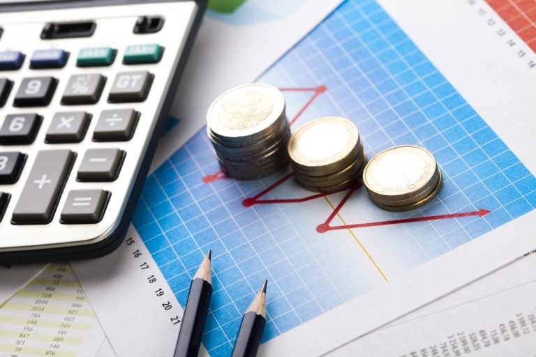 Calculadora, moedas, lápis e gráficos em cima de uma mesa